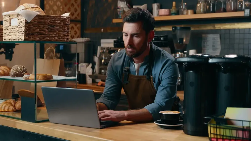 Dueño de una cafetería trabajando en su laptop dentro de su negocio