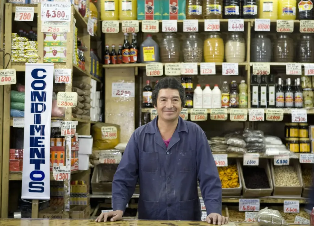 Dueño de un mercado latino sonriendo tras el mostrador de su negocio